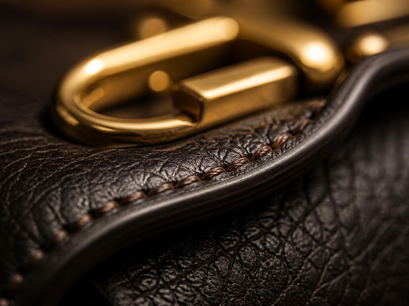 Macro detail of hand stitching along a leather edge with polished hardware behind
